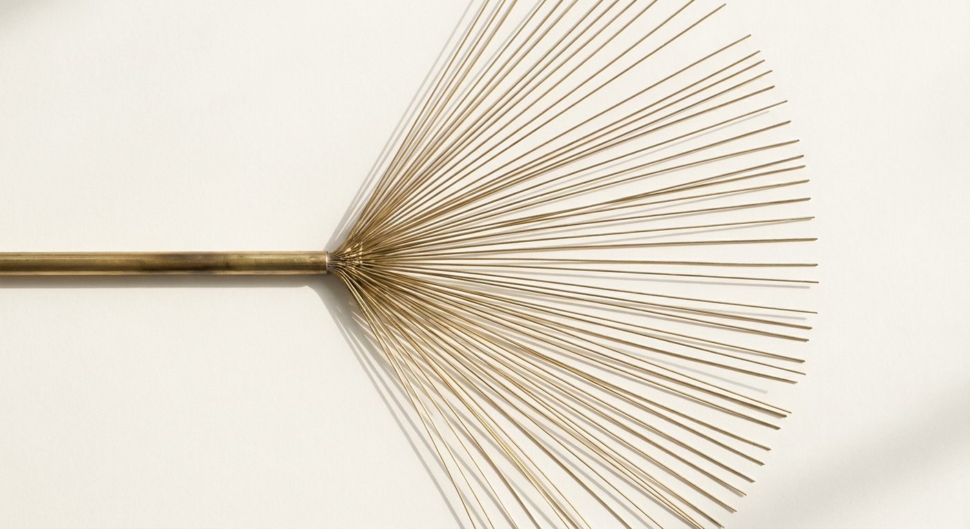 A single brass rod fanning out into dozens of fine brass wires against a warm white surface